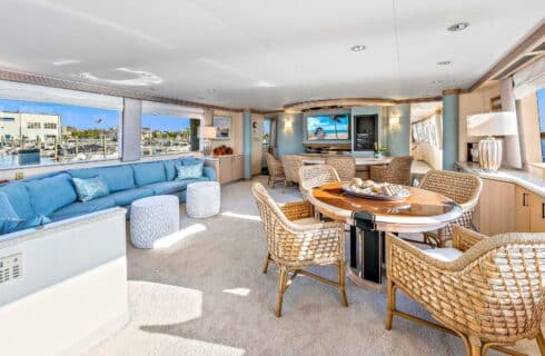 Yacht's salon area with teal upholstered sectional and wooden table with wicker chairs