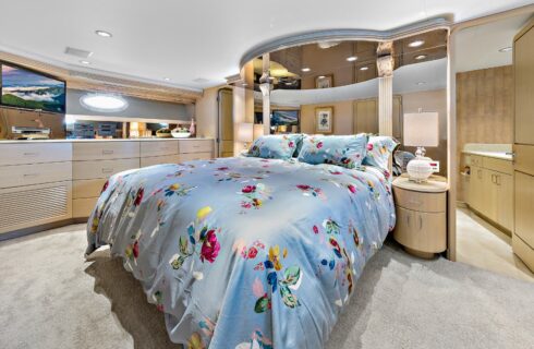 Yacht bedroom with colorful bedding, TV, storage cabinets, and view into bathroom