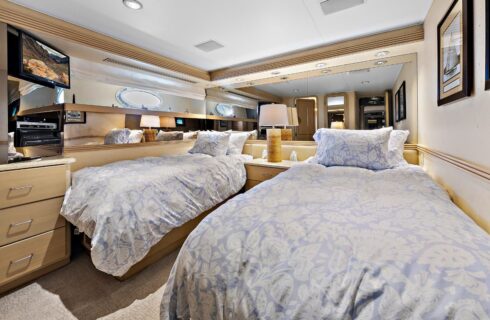 Yacht bedroom with two twin beds, light lavender bedding, storage cabinets, and TV