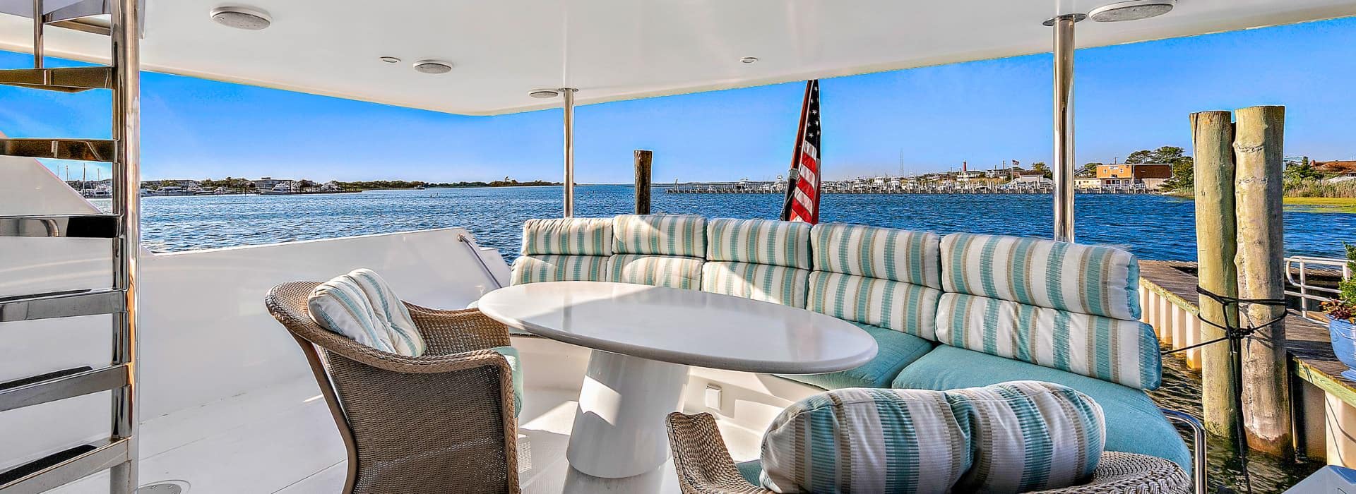 Yacht's aft deck with brown wicker chairs, white table, and seating area with light green cushions