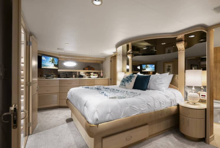 Yacht bedroom with colorful bedding, sofa, desk with chair, storage cabinets, and view into bathroom