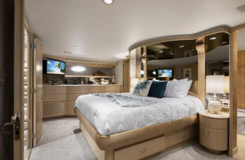 Yacht bedroom with colorful bedding, sofa, desk with chair, storage cabinets, and view into bathroom