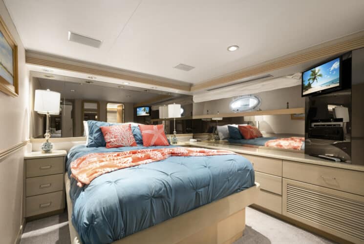 Yacht bedroom with colorful bedding, storage cabinets, and TV