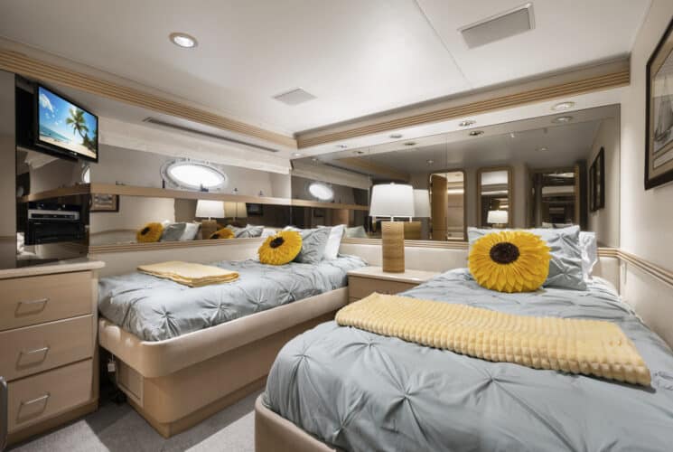 Yacht bedroom with two twin beds, light lavender bedding, storage cabinets, and TV