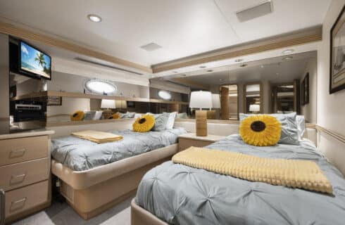 Yacht bedroom with two twin beds, light lavender bedding, storage cabinets, and TV