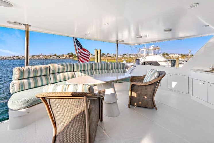 Yacht's aft deck with brown wicker chairs, white table, and seating area with light green cushions