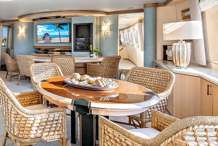 Yacht's salon with bar and game table, brown wicker chairs, and entertainment system