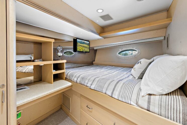 Yacht bedroom with light gray bedding, storage cabinets, and TV