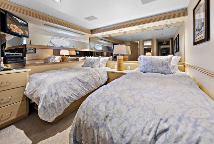 Yacht bedroom with two twin beds, light lavender bedding, storage cabinets, and TV