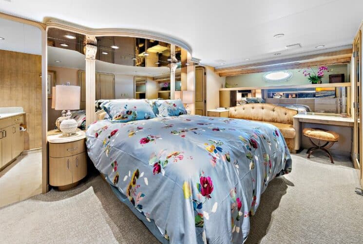 Yacht bedroom with colorful bedding, sofa, desk with chair, storage cabinets, and view into bathroom