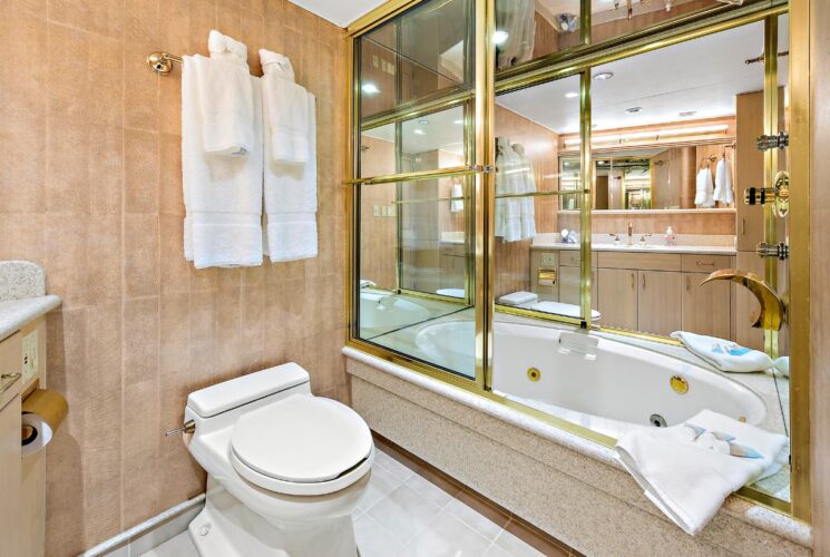 Yacht master bathroom with light colored walls, tiled flooring, light tan vanity, and shower/tub combo with glass and brass shower door