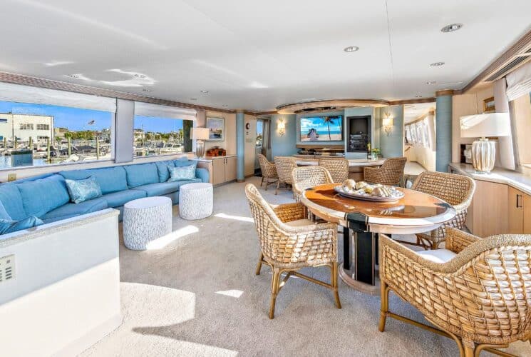 Yacht's salon area with teal upholstered sectional and wooden table with wicker chairs