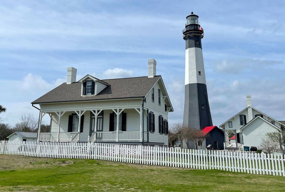 White buildings and black and white lighthouse surrounded by white picket fence