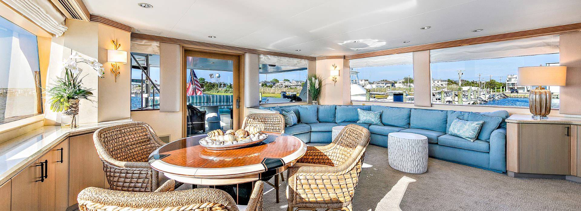 Yacht's salon area with teal upholstered sectional and wooden table with wicker chairs
