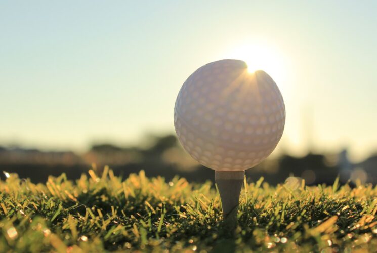 Close up view of a golf ball on a tee with the sun in the background